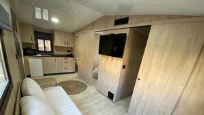 A compact living space with a sofa, kitchenette, and a TV mounted on a wall.