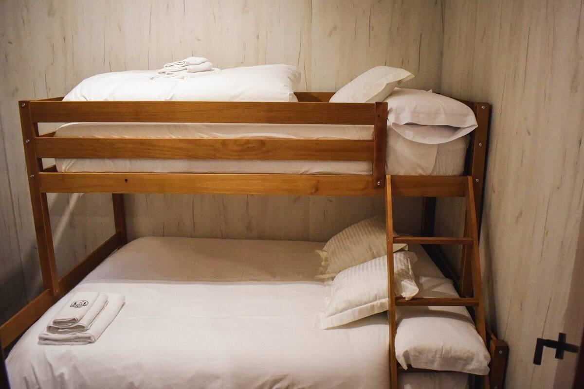 A bunk bed with white bedding and towels, wooden headboard, and a ladder.