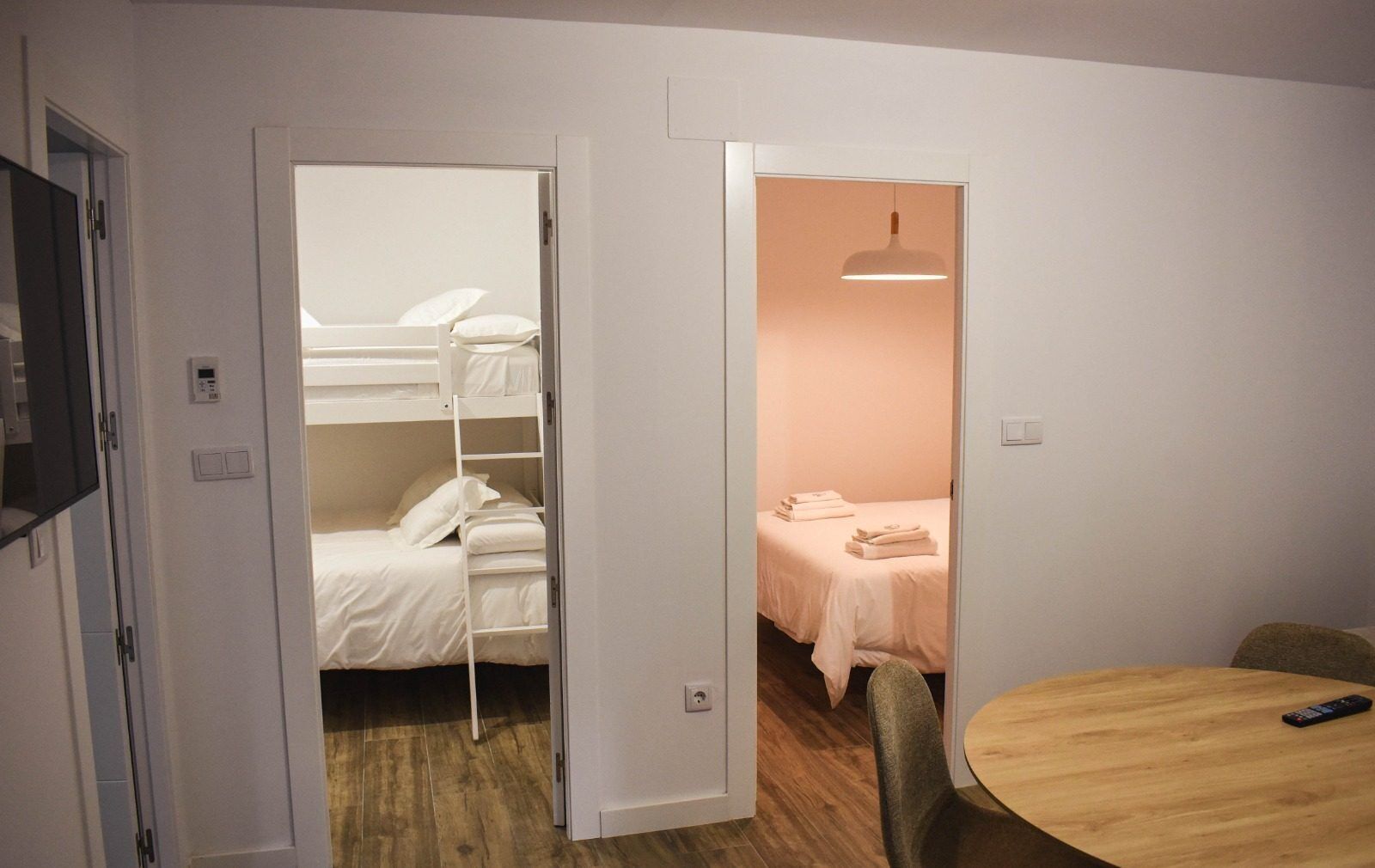 Ein Zimmer mit Etagenbetten, einem kleinen Tisch mit Fernbedienung und einem separaten Bett mit Handtüchern.