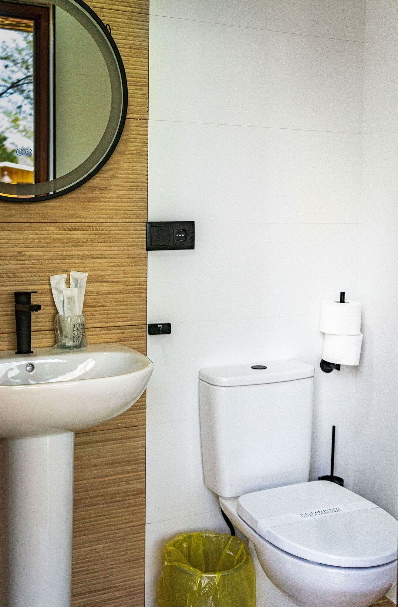 Un baño con lavamanos blanco, inodoro, espejo y cubo de basura.