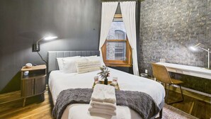 Quarto com cama, mesa de cabeceira, abajur e escrivaninha com cadeira.