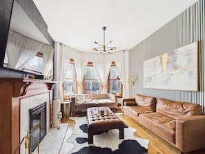 Ein modernes Wohnzimmer mit Kamin, Ledersofas, einem großen abstrakten Gemälde und Blick ins Freie.