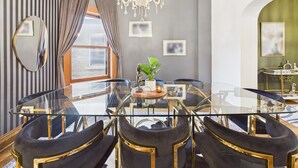 Uma sala de jantar com mesa de vidro e cadeiras pretas com detalhes dourados, um candelabro e papel de parede listrado.