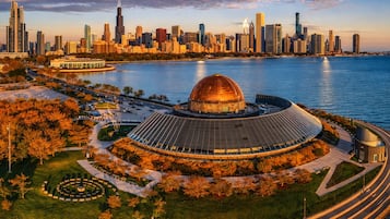 A modern building with a large dome and circular design, surrounded by a landscaped area with trees and a water body.