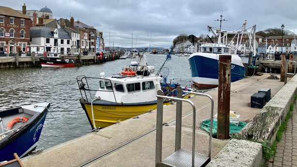 A harbor with boats docked, a building labeled 'The George Inn', and a cloudy sky. - Brewery View (Weymouth)