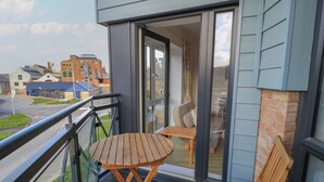 A balcony with a wooden table and two chairs, overlooking a street with buildings. - Brewery View (Weymouth)