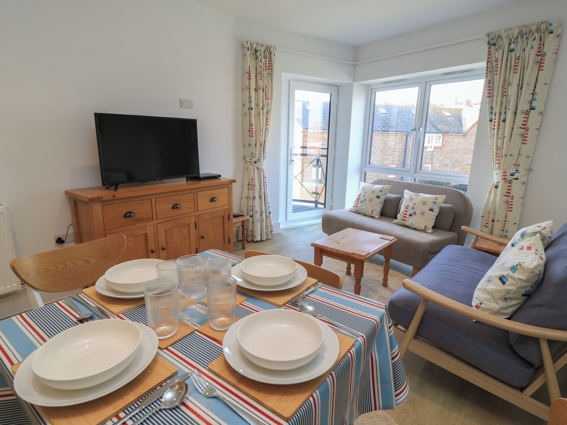A living room with a dining table set for four, a sofa, a television, and a window with curtains.