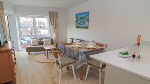 A dining area with a table set for two, a sofa, and a view of the street outside. - Brewery View (Weymouth)