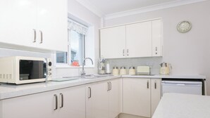 Una cocina compacta con armarios blancos, microondas, tostadora y hervidor.
