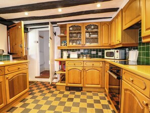 A kitchen with wooden cabinets, a microwave, and a checkered floor. - Hop Cottage (Petersfield)