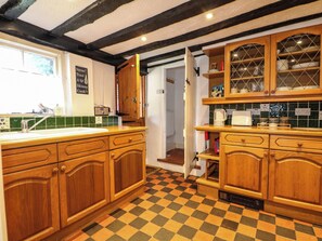 A kitchen with wooden cabinets, a checkered floor, and a window. - Hop Cottage (Petersfield)