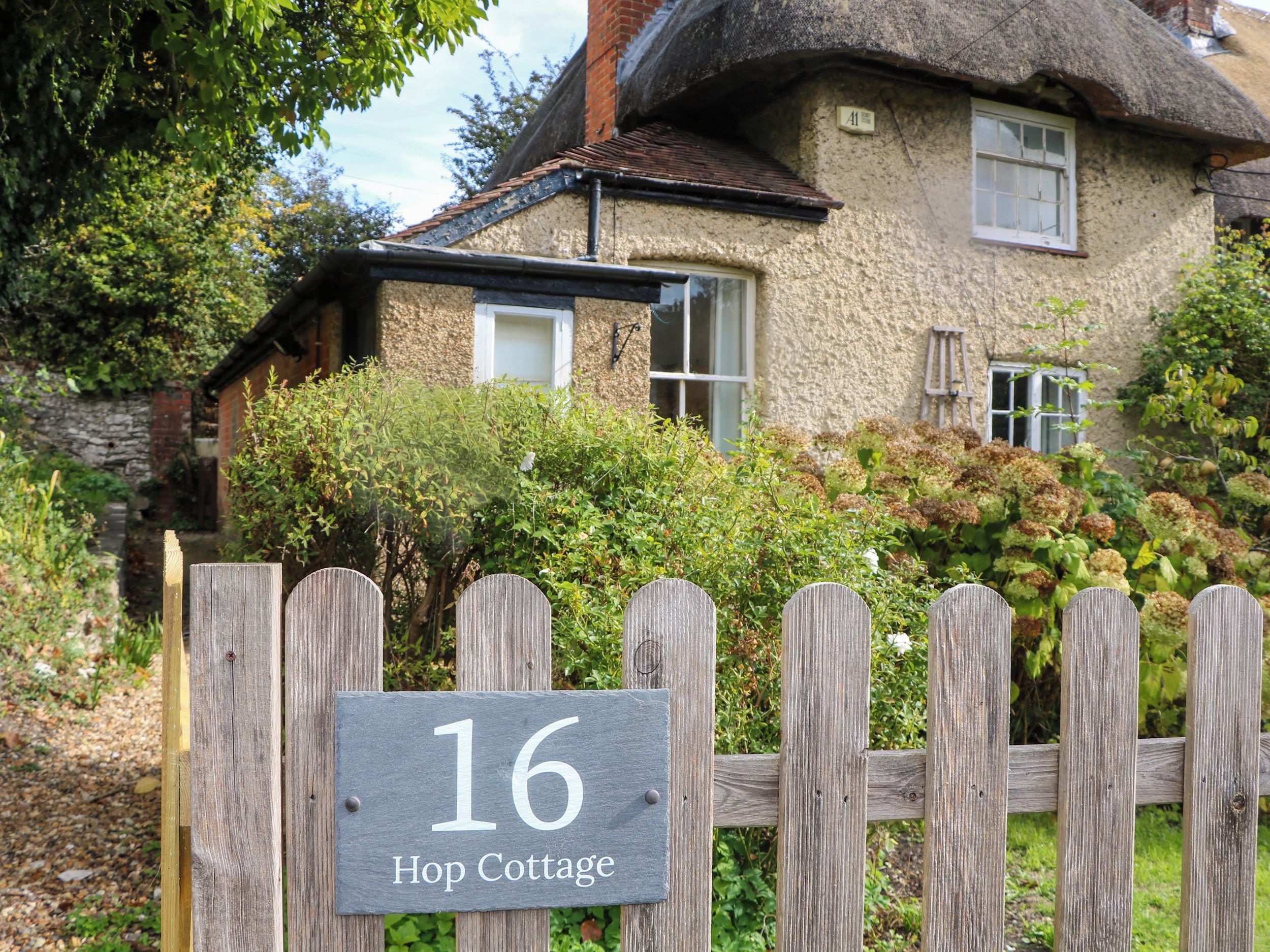 Ein Ferienhaus mit Strohdach, einem Holenzaun und einem Schild, das '16 Hop Cottage' anzeigt.