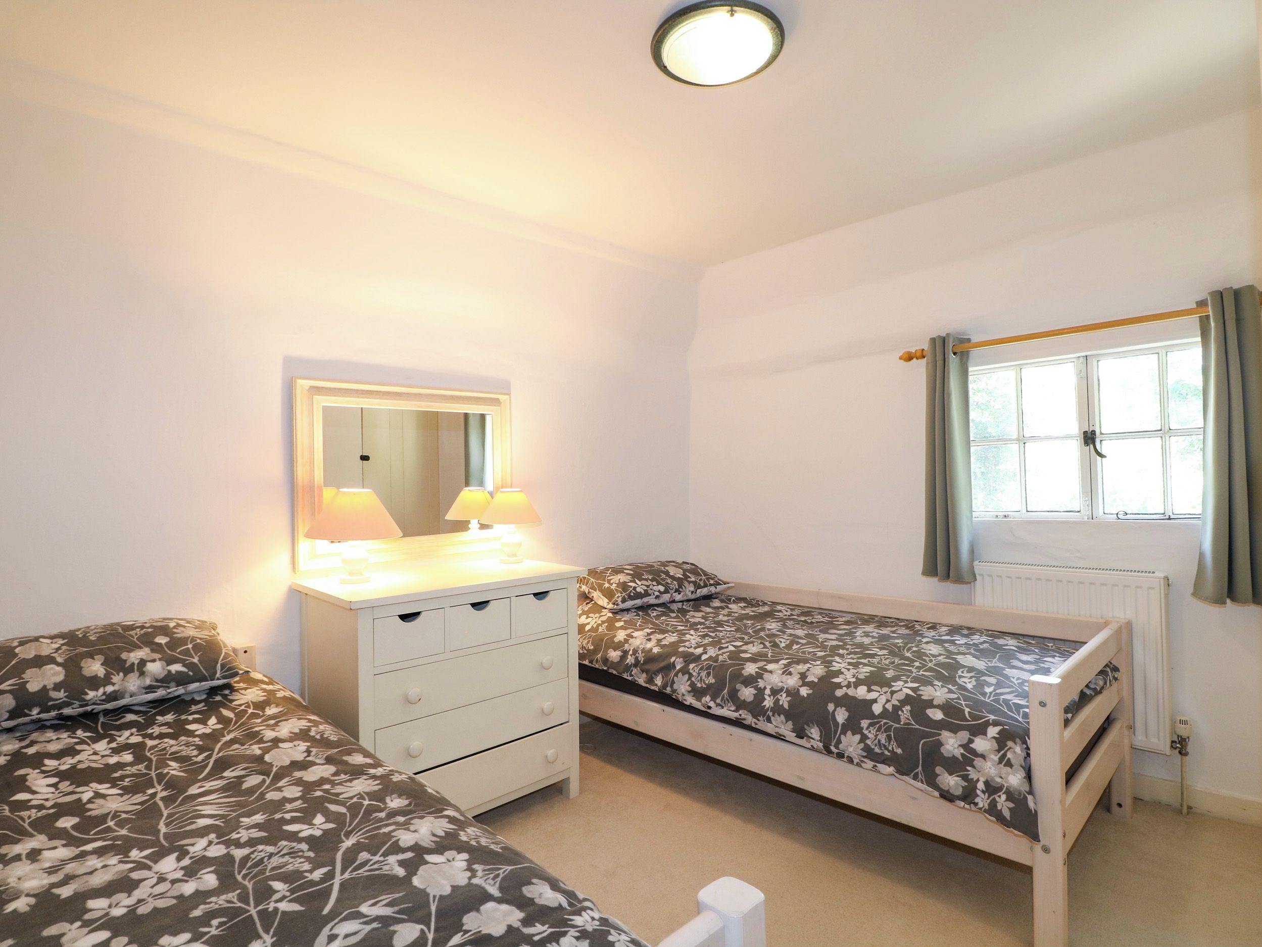 A bedroom with two single beds, a dresser, a mirror, and a window with curtains.