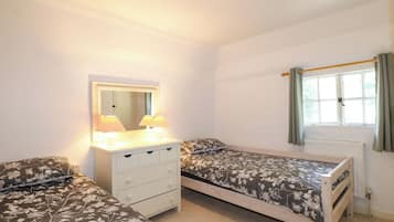 A bedroom with two single beds, a dresser, a mirror, and a window with curtains.