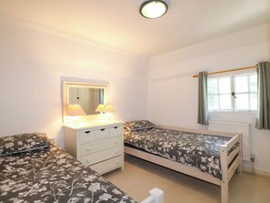 A bedroom with two single beds, a dresser, a mirror, and a window with curtains. - Hop Cottage (Petersfield)