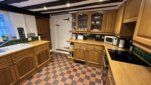 A kitchen with wooden cabinets, a black and orange checkered floor, and a microwave. - Hop Cottage (Petersfield)
