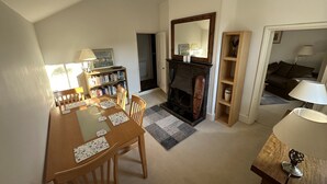 A dining area with a wooden table and chairs, a bookshelf, a fireplace, and a mirror. - Hop Cottage (Petersfield)