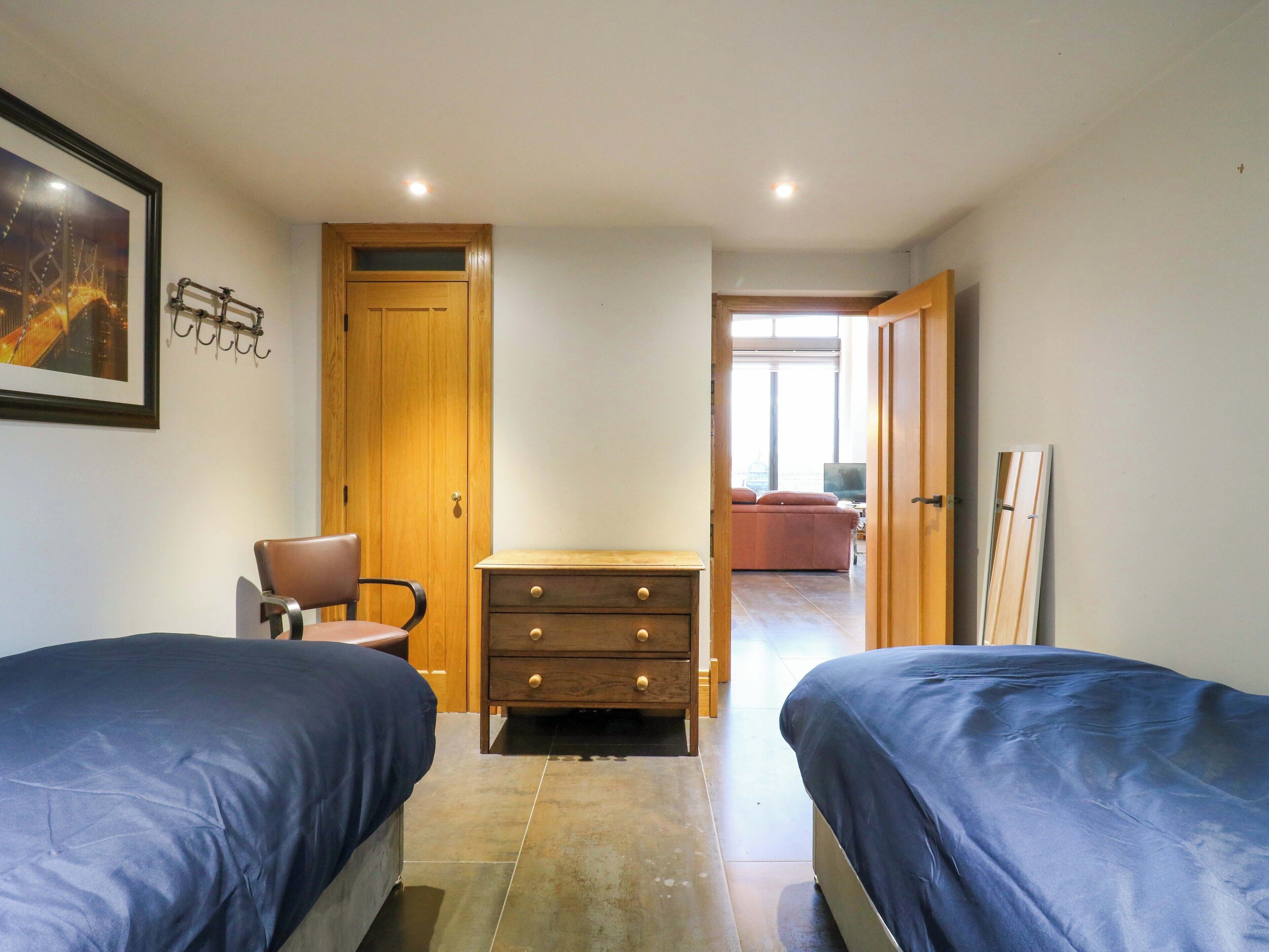 A bedroom with two beds, a wooden dresser, a chair, and a door leading to another room.