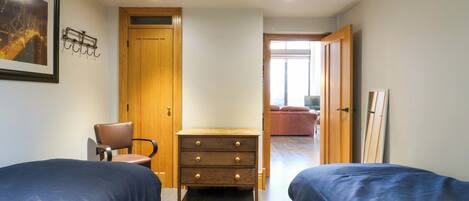 A bedroom with two beds, a wooden dresser, a chair, and a door leading to another room.