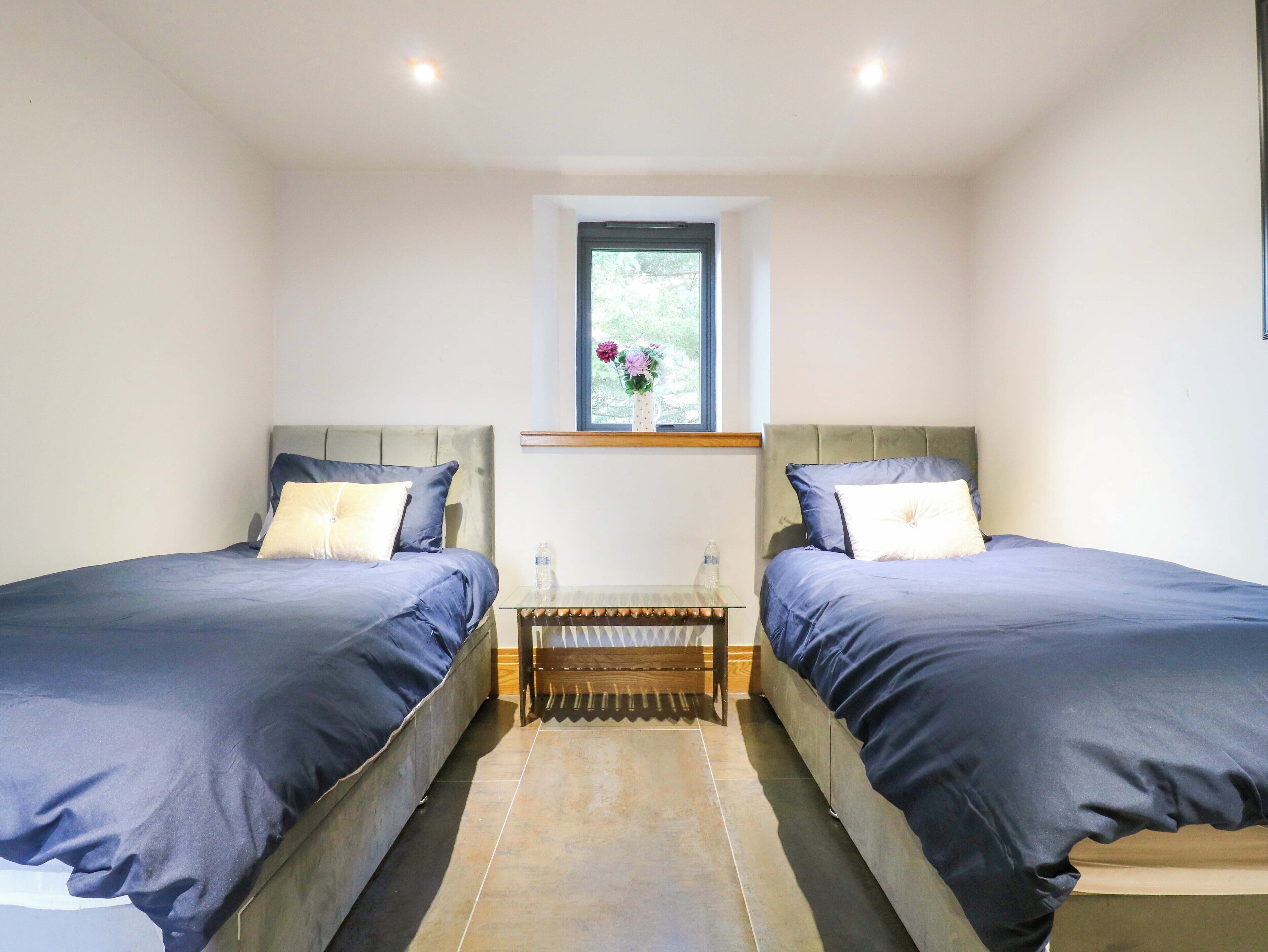 A bedroom with two beds, a small window with a view, and a wooden bench between the beds.