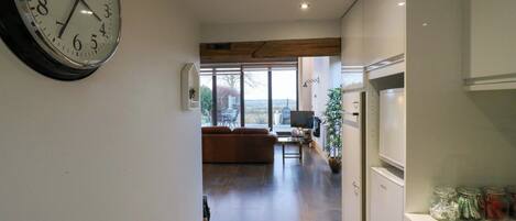 A modern kitchen with a clock, a dining area with a sofa, and a view through the window.