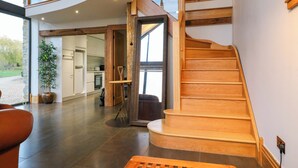Un interior espacioso con una escalera de madera, una planta grande en maceta y vistas a la cocina a través de una puerta abierta.