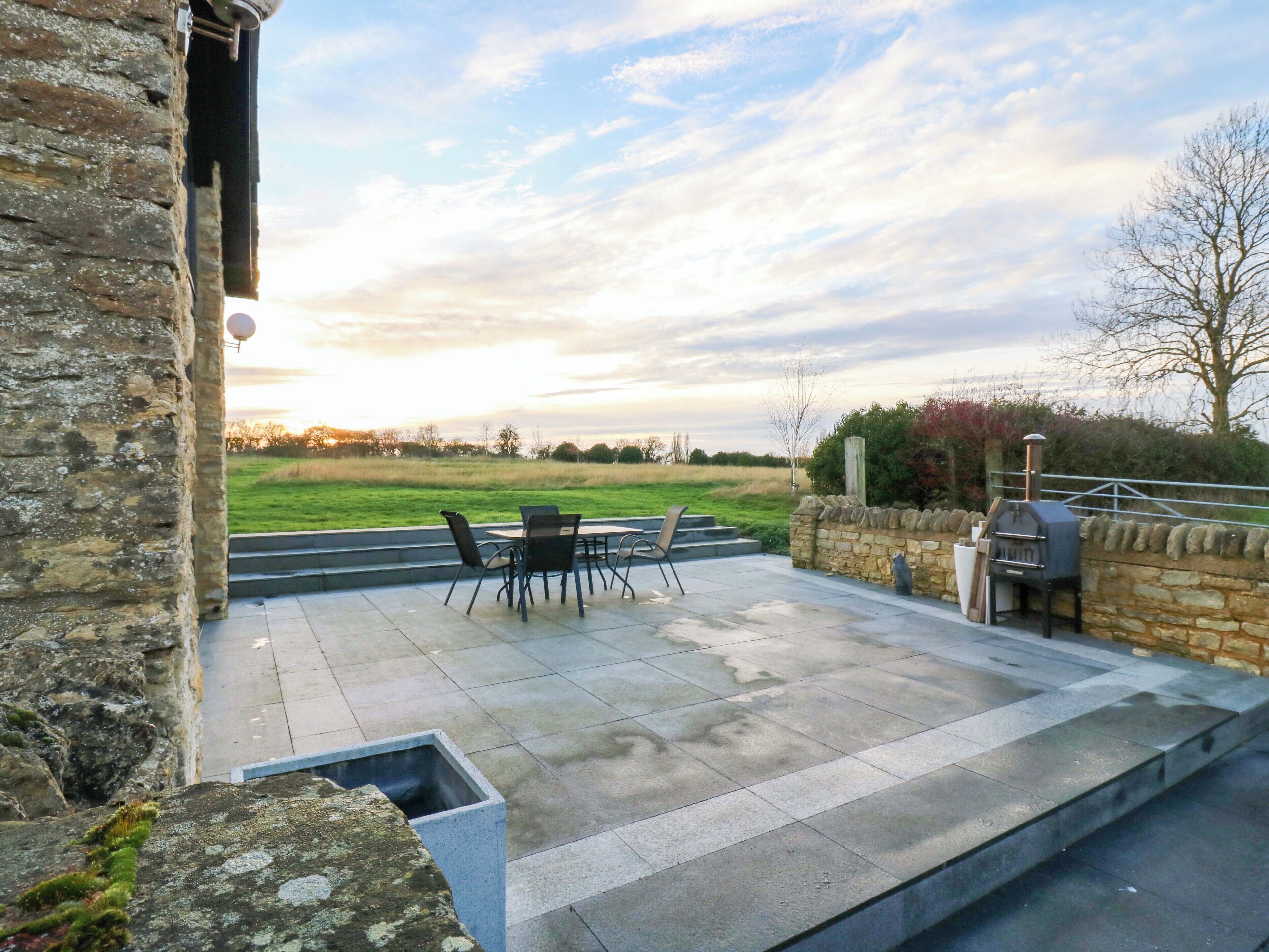 Une terrasse avec des murs en pierre, un barbecue et une vue sur la campagne.