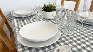 Una mesa de comedor cubierta con un mantel a cuadros, con platos blancos, vasos y una pequeña planta en maceta.