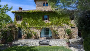 A stone building with ivy, a stone patio, and a bench.