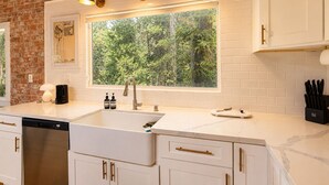 A kitchen with a large window, white cabinetry, and a dishwasher.