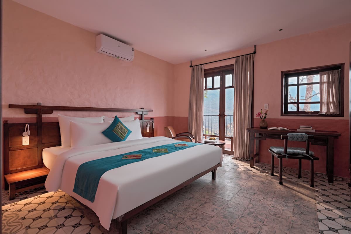 A hotel room with a bed, a desk, a chair, a window, and a balcony.