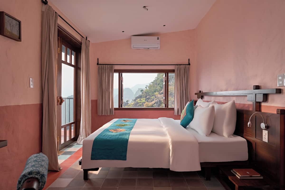 A hotel room with a bed, a window with curtains, a ceiling fan, and a view of the outdoors.