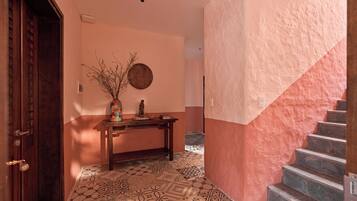 A hallway with patterned floor tiles, a wooden door, a small table with a vase, and a staircase with a pink wall.