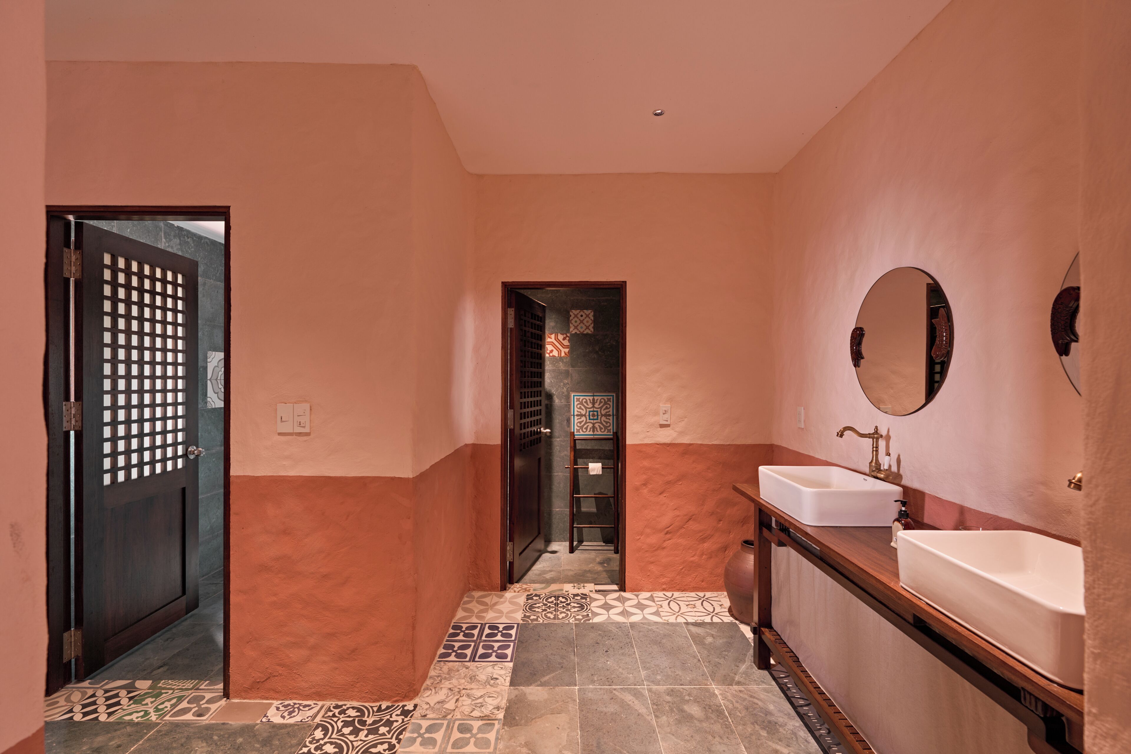A bathroom with a tiled floor, a sink, a mirror, and a door with a decorative screen.