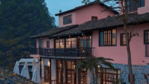 A pink villa with a balcony, stone walls, and a stone pathway. - Ha Giang Aya Lodge (Lung Phin)