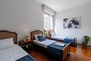 A hotel room with three beds, a large window with blinds, a wall-mounted artwork, and a potted plant. - Beira-Mar com 5 Quartos e vista incrível (Guarujá)