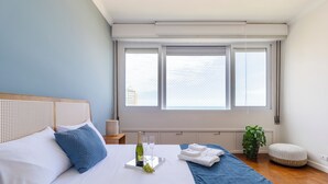 A neatly made bed with white and blue bedding, a bottle of champagne, and glasses on a tray. - Beira-Mar com 5 Quartos e vista incrível (Guarujá)