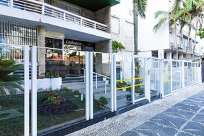A modern building with a glass entrance, a visible address sign, and a small garden area with plants and flowers. - Beira-Mar com 5 Quartos e vista incrível (Guarujá)