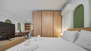 A hotel room with a large bed, a desk with a flat-screen TV, a chair, and a small table.