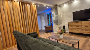 Un salon moderne avec un canapé d’angle, un meuble en bois, un téléviseur à écran plat et un vase décoratif posé sur une table basse en bois.