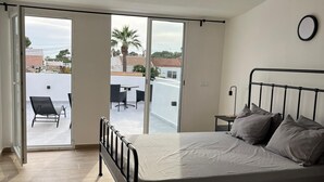 A bedroom with a bed, a nightstand, and a view through a sliding door to an outdoor patio with a table and chairs. - Villa Palma Cabo Roig- Spacious 5-bedroom villa in peaceful Cabo Roig with AC (orihueala costa)