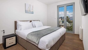 Un dormitorio con cama, mesita de noche, televisor y ventana con vista a la ciudad.