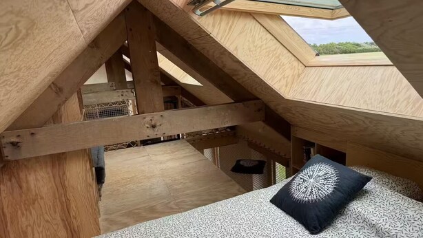 A wooden loft bedroom with a skylight, a patterned bedspread, and a decorative pillow. - Stone house near the ocean (Tréogat)
