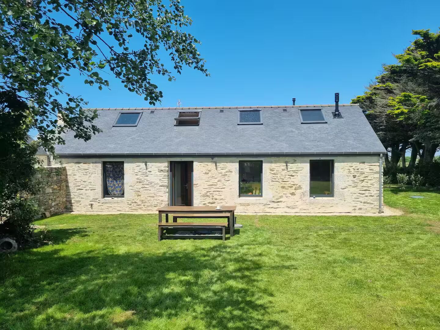 Ein Haus aus Stein mit einem geneigten Dach, einer kleinen Veranda und einem Rasen.