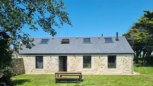 A stone house with a sloped roof, a small front porch, and a grassy yard. - Stone house near the ocean (Tréogat)