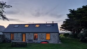 A stone house with a sloped roof, two skylights, and a small patio area. - Stone house near the ocean (Tréogat)