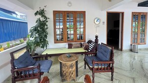 A spacious room with a large window, a wooden sofa set, a small round table, and a potted plant. - Water Element Cozy 1-bedroom villa in fantastic Thiruvananthapuram with AC (Thiruvananthapuram)