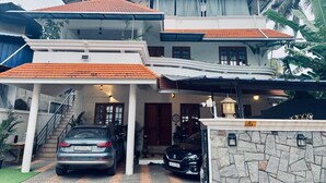 A two-story house with a covered driveway, a staircase leading to the upper floor, and a car parked in the driveway. - Water Element Cozy 1-bedroom villa in fantastic Thiruvananthapuram with AC (Thiruvananthapuram)