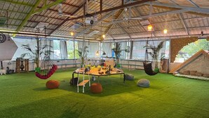 A spacious indoor area with a high ceiling, artificial grass flooring, hanging chairs, and a central table with various items. - Water Element Cozy 1-bedroom villa in fantastic Thiruvananthapuram with AC (Thiruvananthapuram)