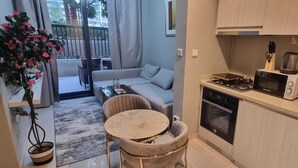 Eine kompakte Küche mit Mikrowelle, Toaster und Backofen. Angrenzend an die Küche befindet sich ein Essbereich mit einem runden Tisch und zwei Stühlen.